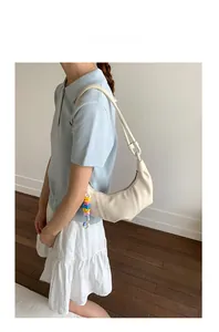 Side view of cream half-moon bag with colorful beaded charm worn by a model