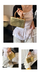 Detail of golden box clutch with pleated metal texture and faux bamboo handle
