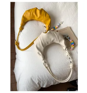 Detail of pleated crescent crossbody bags in yellow and beige with knotted strap detail