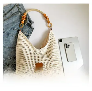 Detail view of cream knit tote bag with wooden bead handle and brown leather logo tag