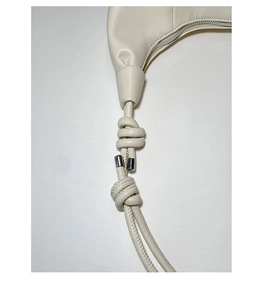 Close-up of knotted leather strap detail and silver metal accent on off-white crossbody bag