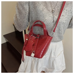 Detailed macro view of bright red faux crocodile texture bucket bag with bear pendant