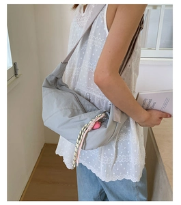 Detail of light grey nylon crossbody bag with wide shoulder strap and heart pendant accessory