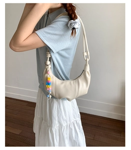 Close-up of cream crescent underarm bag featuring soft pleated texture and bead charm