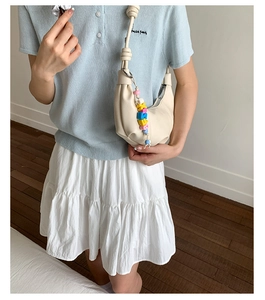Detail of creamy white crescent shoulder bag featuring colorful letter bead charm accessory