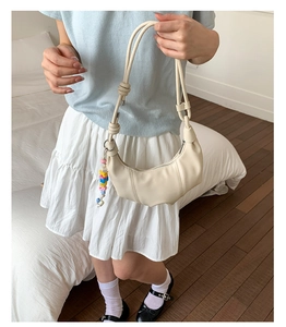 Detail of off-white croissant bag with vertical pleats and colorful beaded charm