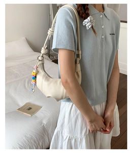 Detail of off-white croissant shoulder bag with colorful beads and knotted strap on model