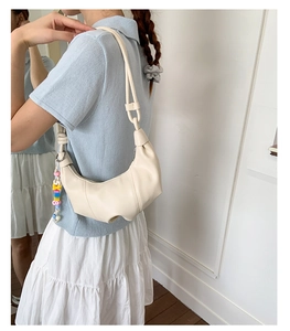 Close-up of beige croissant bag featuring textured pleats and colorful beaded charm