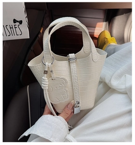 Macro detail of creamy white crocodile pattern bucket bag with bear charm and silver lock