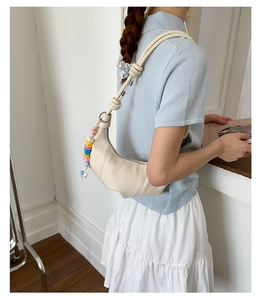 Detail view of cream hobo bag with knotted strap and colorful beads on a model