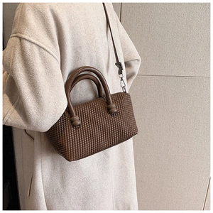 Détail d'un sac cabas marron foncé tissé avec poignées sur un manteau beige chic