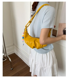 Detail of yellow crescent shoulder bag with colorful beaded charm and pleated leather texture