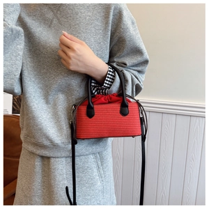 Detail of red straw woven bag featuring black leather handles and drawstring interior