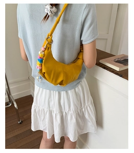 Detail of yellow pleated moon bag with colorful letter pendant on model