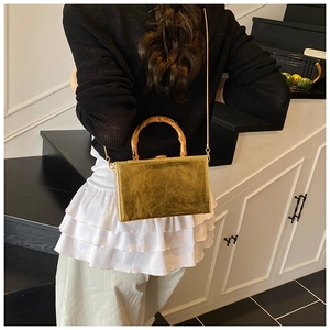 Detail of a gold box clutch featuring a natural bamboo handle and thin metal chain strap