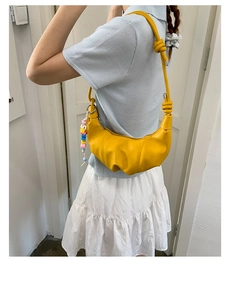 Detail of a vibrant yellow pleated croissant bag with knotted strap and colorful bead charm