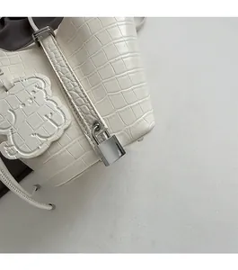 Detail of white crocodile pattern handbag with silver metal lock and bear charm