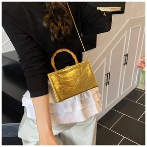 Detail of golden textured mini bag with natural bamboo handle and metal chain