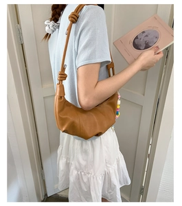 Detail showing brown faux leather croissant bag with knotted strap on a person's shoulder