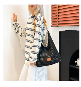 Detail of black hollow knit tote bag with wooden bead strap and orange leather patch