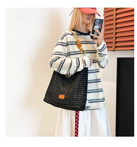 Detail of a black woven tote bag with round wooden beads and orange leather patch