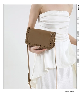 Close-up of brown woven leather flap bag with intricate lacing detail on white dress