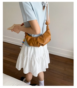 Detailed view of brown croissant bag featuring pleated texture and side knot strap detail