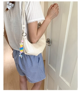 Detail of a minimalist off-white crescent underarm bag with a colorful beaded charm