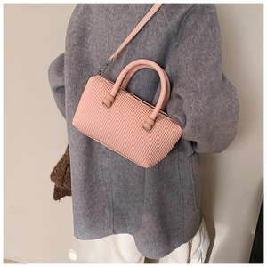 Détail du sac bandoulière rose avec texture alvéolée porté par un mannequin en studio