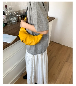 Detail of yellow crescent shoulder bag with pleated leather texture in a lifestyle setting