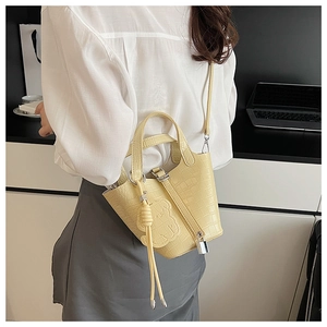 Detail view of yellow faux leather bucket bag with crocodile texture and bear relief charm