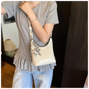 Détail d'un sac à bandoulière beige brillant avec pendentif étoile de mer et nœud décoratif