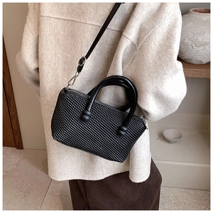 Detailed view of black woven texture handbag with shoulder strap on beige coat model