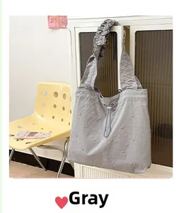 Detail view of grey tote bag with pleated straps, drawstring closure and pearl accents