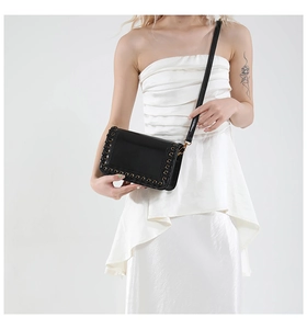 Detail of black glossy leather bag with metal eyelets and woven edge on white dress