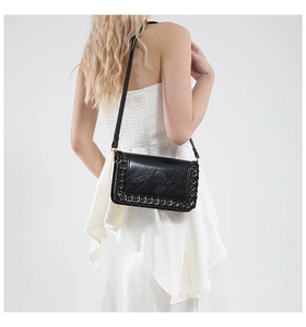 Detail of woven leather edges with gold metal eyelets on a black crossbody bag worn by model