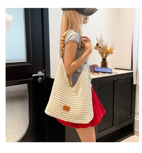 Detail of hollow knit tote bag with yellow wooden bead strap and leather patch