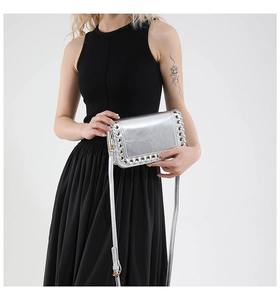 Detail of silver metallic crossbody bag featuring decorative eyelet weaving and slim strap