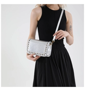 Detail of silver metallic woven crossbody bag with punk style eyelets and gold hardware