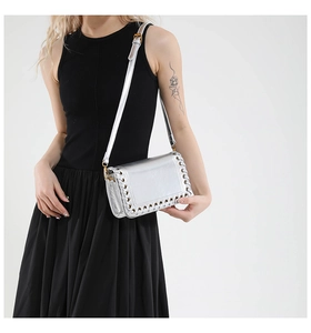 Detail of silver metallic crossbody bag featuring woven perforated edge design on a black dress