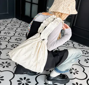 Detail of off-white pleated tote bag featuring shimmering rhinestones and frilled strap