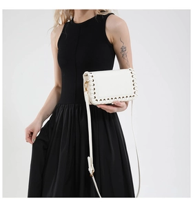 Close-up of white woven square bag with metal eyelets and adjustable shoulder strap