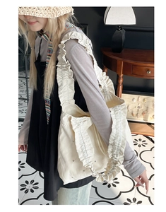 Detail der cremefarbenen Tragetasche mit Rüschengurt und Nietenverzierung am Outfit