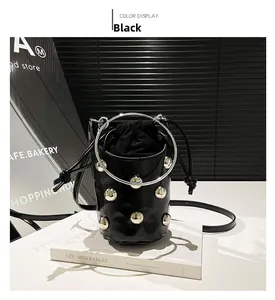 Détail d'un sac seau noir punk avec rivets argentés et poignée anneau sur des livres blancs