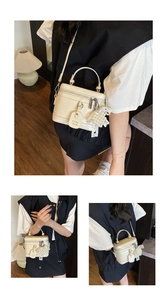 Detail of cream white tote bag featuring pearl lace pendant and metal strap buckle