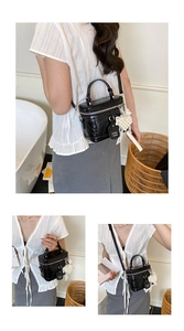 Detail of black patent leather crossbody bag with oversized white pearl tassel and silver hardware