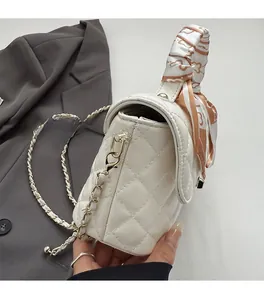Close-up of quilted pattern leather on white handbag with silk scarf and gold chain