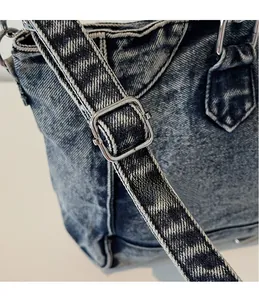 Détail de la boucle en métal argenté et de la bandoulière tisée du sac en jean délavé