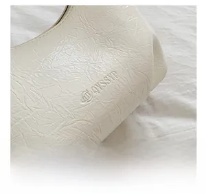 Gros plan d'un sac en cuir plissé blanc crème montrant le logo de la marque embossé