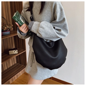 Detail of black hobo bag with litchi texture and adjustable strap in cozy room setting